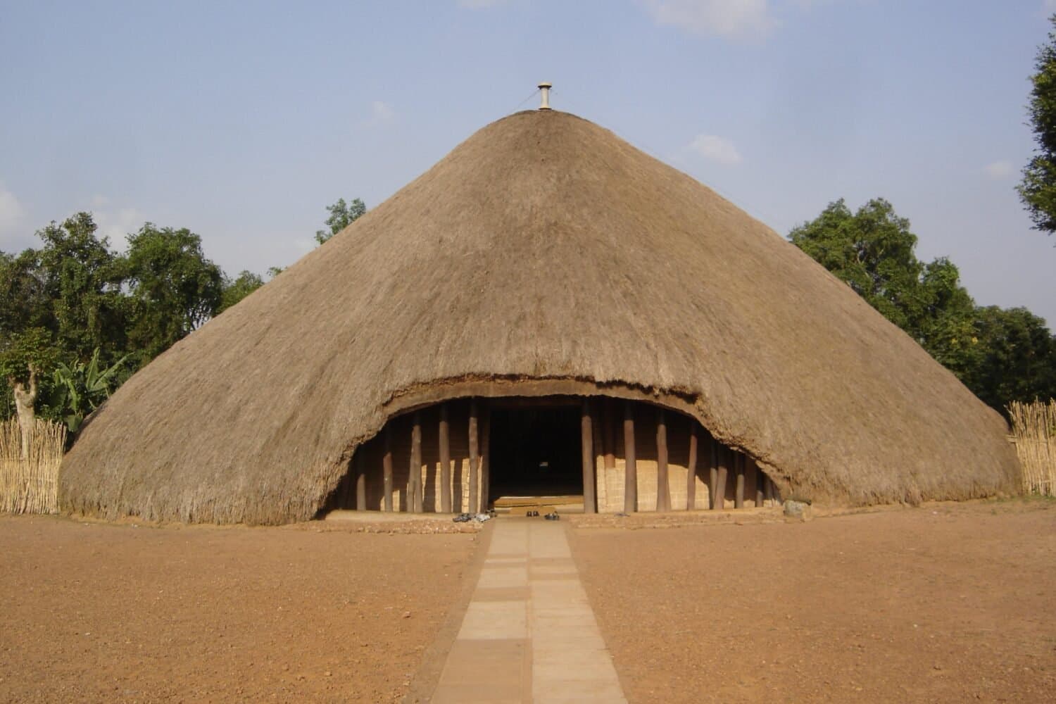 Archive photograph of the thatched royal tomb building at Kasubi, with a path leading to its entrance.